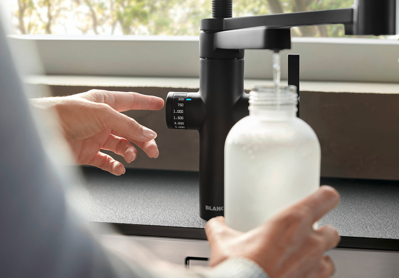 Detail of the "Click & Drink" rotary dial on the BLANCO EVOL-S Pro Filter tap, being used to pre-set a precise volume of filtered water for a glass bottle.