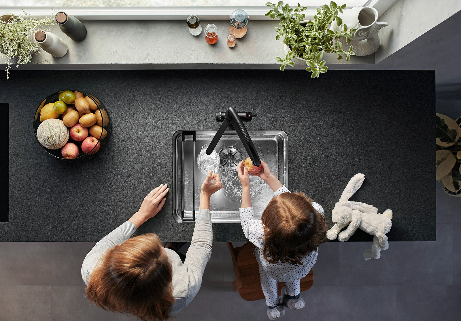 Overhead view of a mother and child at a stainless steel sink using the BLANCO EVOL-S Pro Filter tap in Black Matt for safe, filtered drinking water and food preparation