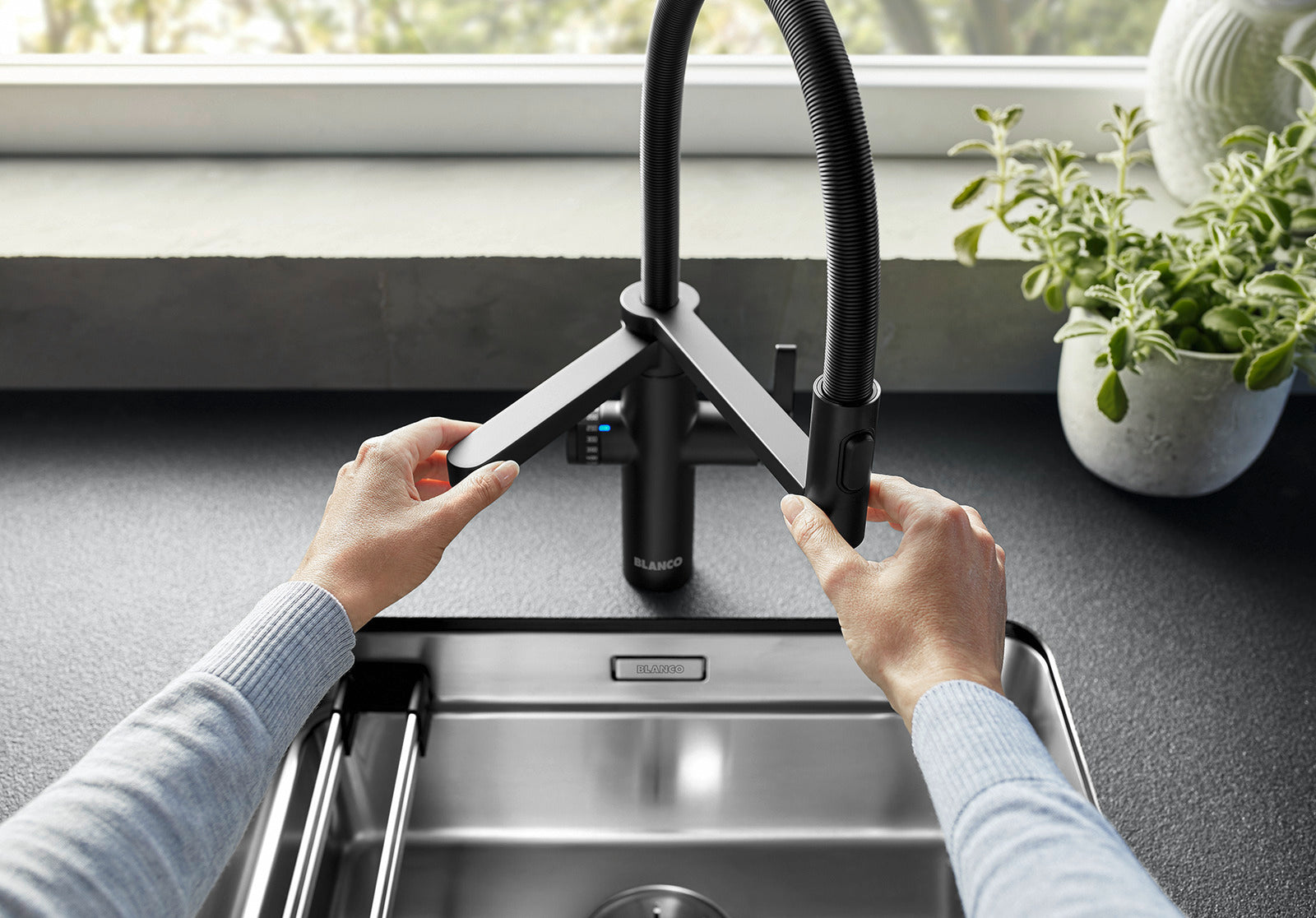 Hands demonstrating the two-in-one functionality of the Black Matt BLANCO EVOL-S Pro, showing the flexible mixer spout and the dedicated horizontal purified water spout.