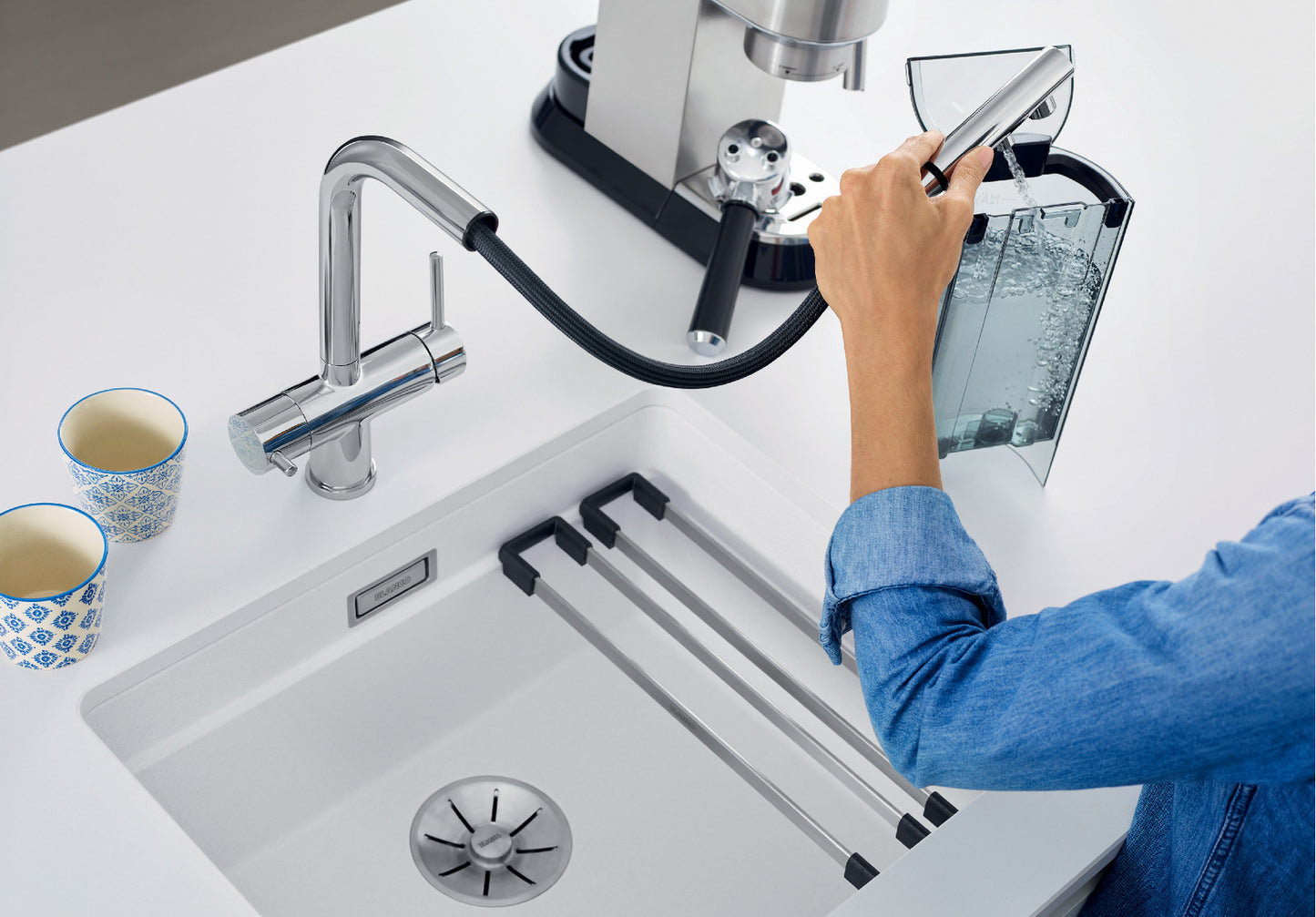 Action shot of the BLANCO Fontas-S II Chrome Mixer, illustrating its flexible pull-out spout function. A user extends the hose to easily fill an espresso machine’s external reservoir located at the edge of the kitchen counter, showing the Fontas-S II's extended operational radius