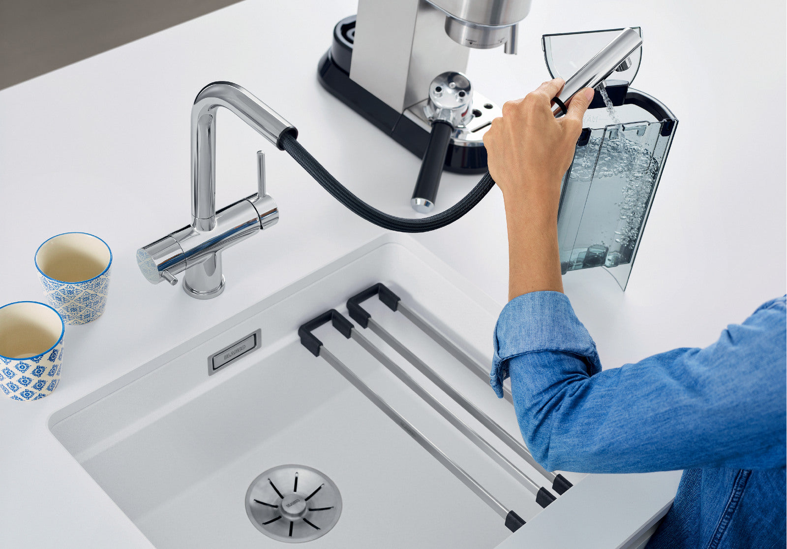 Action shot of the BLANCO Fontas-S II Chrome Mixer, illustrating its flexible pull-out spout function. A user extends the hose to easily fill an espresso machine’s external reservoir located at the edge of the kitchen counter, showing the Fontas-S II's extended operational radius