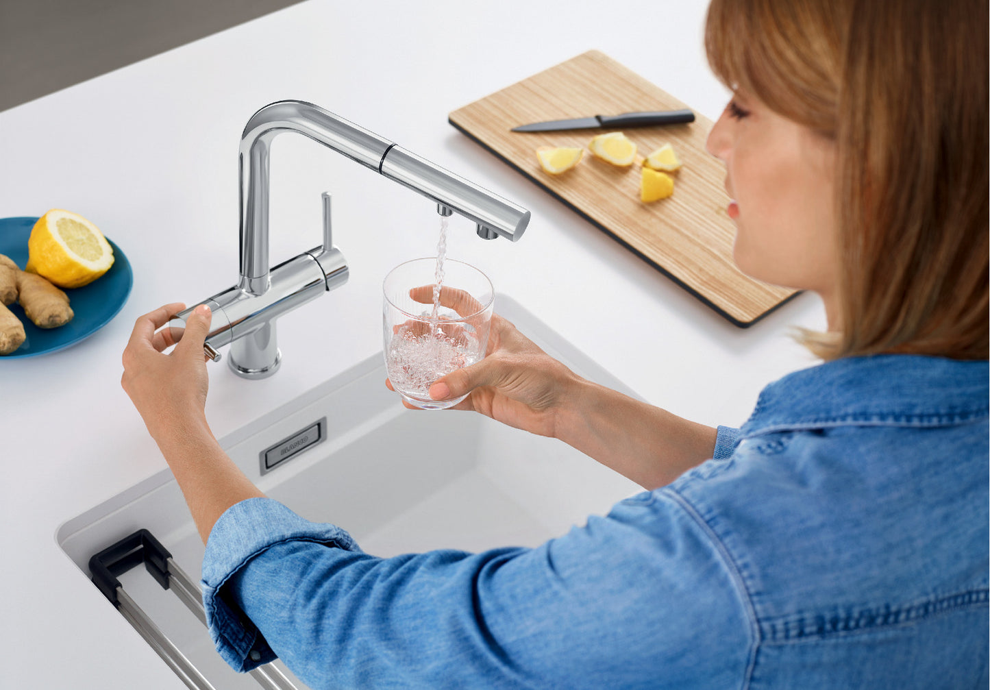 Action shot demonstrating a user dispensing purified water directly from the BLANCO Fontas-S II Filter Mixer. The separate control lever on the left base ensures a distinct stream of drinking water, making it a true 3-in-1 filtered kitchen solution